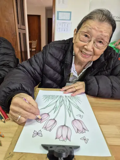 Senhora de óculos colorindo um desenho de tulipas com lápis de cor