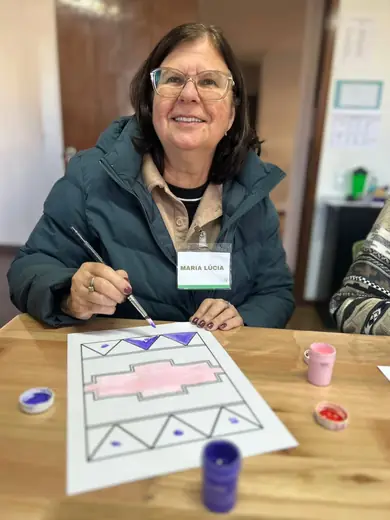 Senhora de óculos pintando com tinta um desenho de formas geométricas