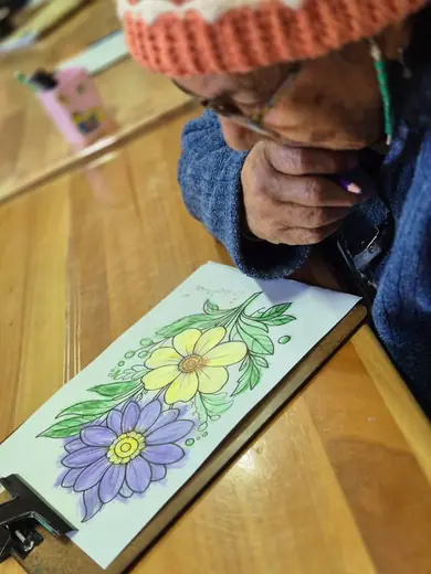 Mãos de um senhor de touca de lã pintando um desenho de flores na prancheta