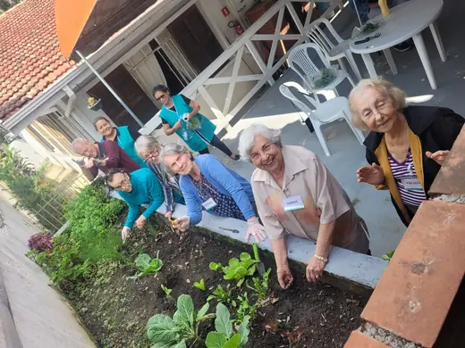 Idosos e equipe agachados em volta do canteiro da horta, sorrindo para a foto